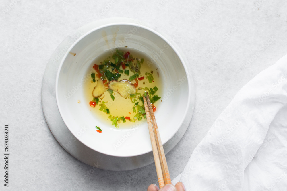 Overhead view of Slices of red green chilli and oil in a white ceramic bowl, top view of spices chili peppers chopsticks in a white bowl, process of making chili oil Overhead view of Slices of red green chilli and oil in a white ceramic bowl, top view of spices chili peppers chopsticks in a white bowl, process of making chili oil