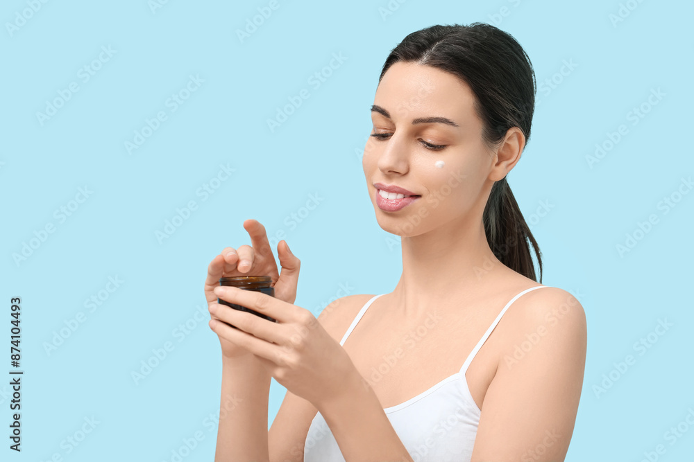 Beautiful young woman with jar of face cream against blue background Beautiful young woman with jar of face cream against blue background