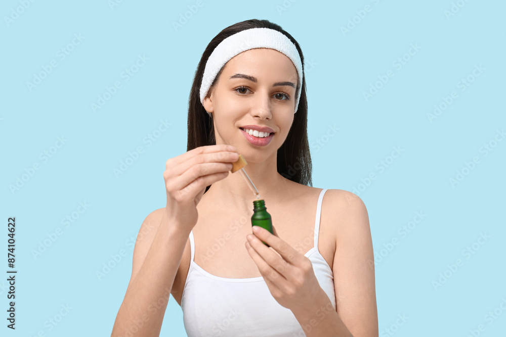 Beautiful young woman with bottle of face serum on blue background Beautiful young woman with bottle of face serum on blue background
