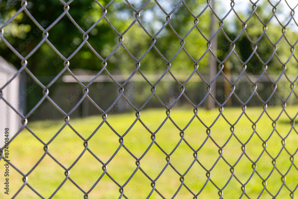 Chain link fence in the foreground with a lawn and trees in the background. Chain link fence in the foreground with a lawn and trees in the background.