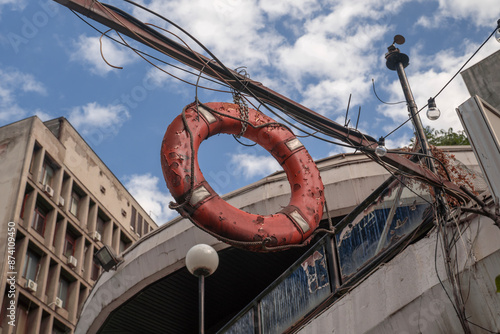 An old red lifebuoy is hanging in the city suspended from wires. A pier with fishing boats. High quality photo