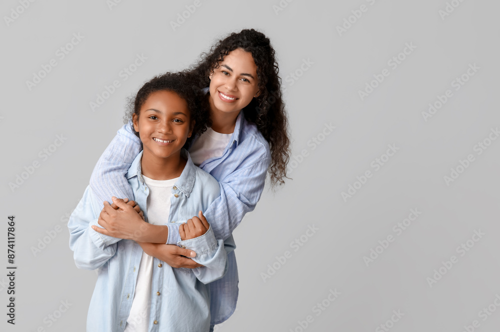 Beautiful young happy African-American mother with her daughter hugging on grey background Beautiful young happy African-American mother with her daughter hugging on grey background