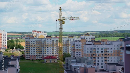 Working crane on construction set of building with heavy house panel on it pull it down to worker at building. Sunny Day. Field At The Background