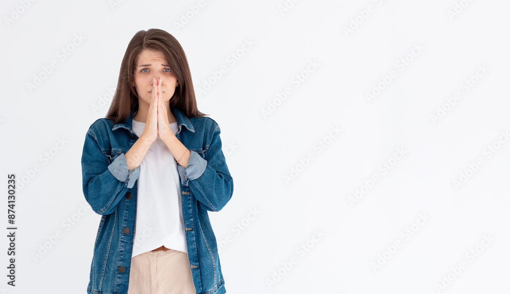 Portrait of imploring girl tilts head, purses lips, looks sadly at camera, makes praying gesture, asks for help and support, begs boyfriend for apologize, isolated on white wall Portrait of imploring girl tilts head, purses lips, looks sadly at camera, makes praying gesture, asks for help and support, begs boyfriend for apologize, isolated on white wall