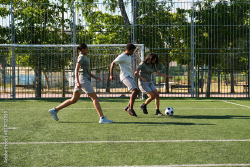 Obraz na płótnie Three young soccer players are running on artificial turf during training session w salonie
