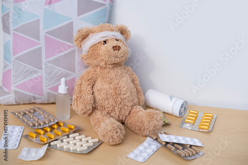 teddy bear with bandaged head, surrounded by scattered medicines and pills, health, care and treatment children through soft toy, medical therapy and pediatrics photo