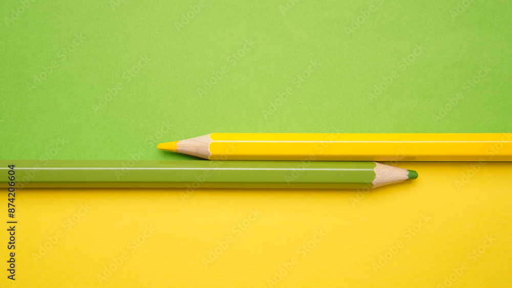 Two pencils are on a yellow and green background Two pencils are on a yellow and green background