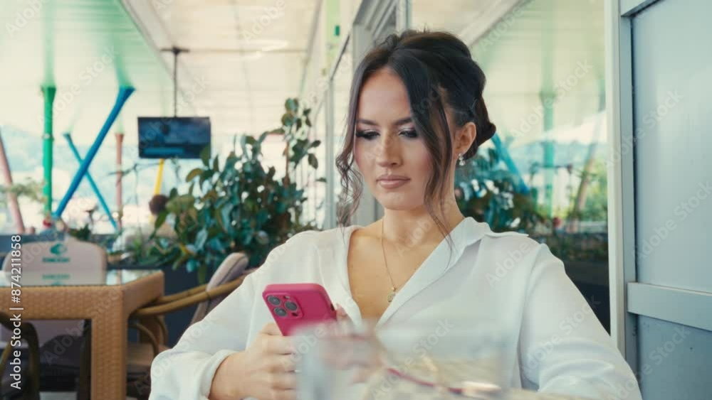 Close-up of a Serious Pretty Caucasian Young Woman Using a Smartphone in a Cafe Restaurant. She appears concerned, anxious, worried. The setting is modern and casual Close-up of a Serious Pretty Caucasian Young Woman Using a Smartphone in a Cafe Restaurant. She appears concerned, anxious, worried. The setting is modern and casual