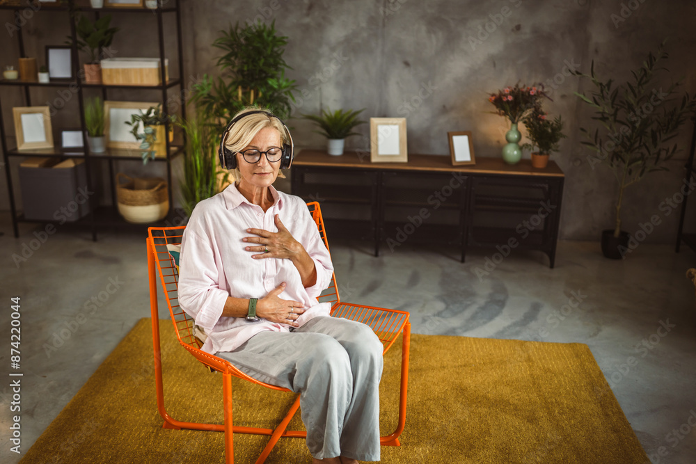 Fototapeta premium Mature woman sit on chair with headphones and have guided meditation
