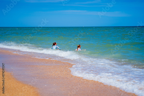 two children, a red-haired girl and a blonde girl on the seashore play in the waves and run along the beach on the sand, sit in the water in nature