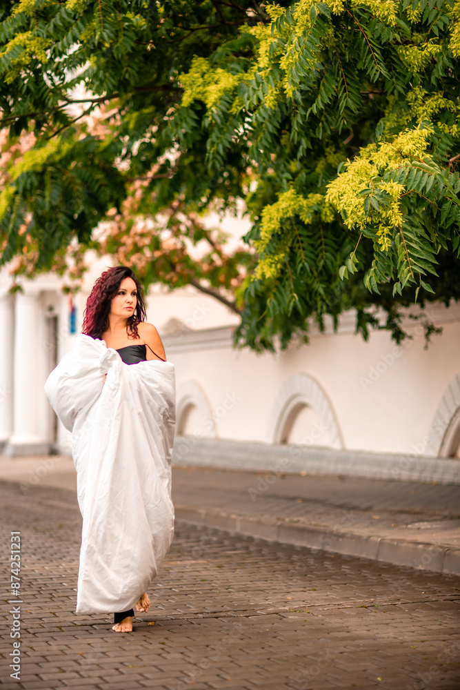 Naklejka premium Woman city blanket. Morning in the big city. A blonde woman in a white blanket is enjoying in the city center. Photographed for social media
