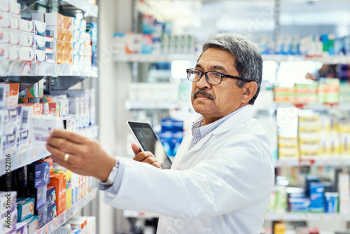 Pharmacist, tablet and pills in stock, inventory and medicine as chemist, drugstore and employee. Man, doctor and digital checklist in pharmacy, clinic or dispensary for prescription, help or advice photo