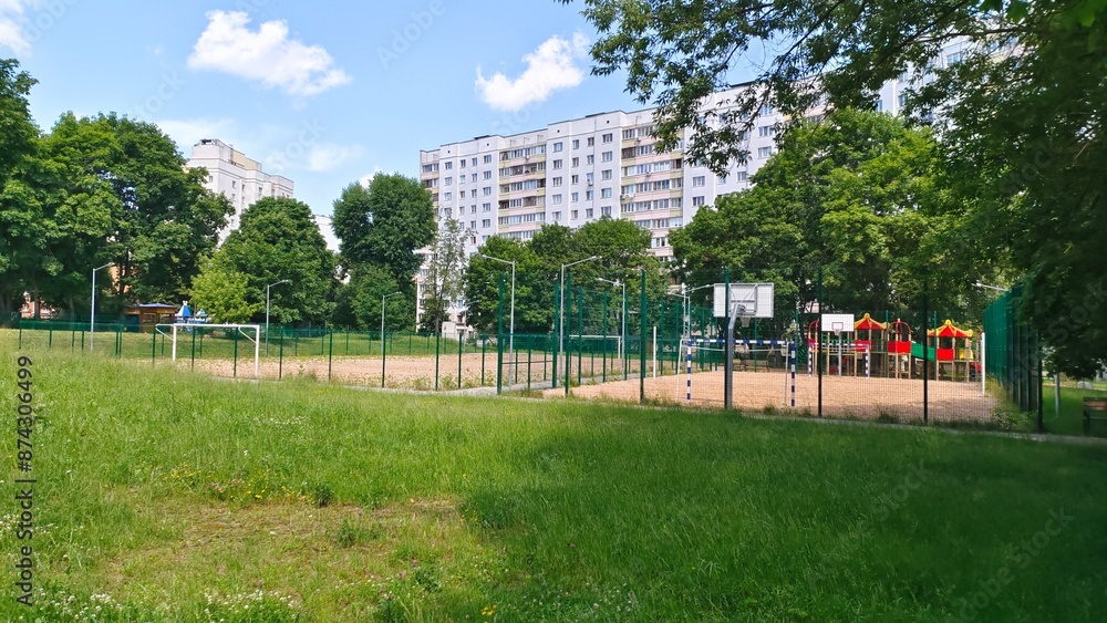 Sandy soccer and basketball courts with metal gates and plastic boards, with poles with lighting lanterns are fenced with a metal mesh fence. Around there are residential houses and trees Sandy soccer and basketball courts with metal gates and plastic boards, with poles with lighting lanterns are fenced with a metal mesh fence. Around there are residential houses and trees