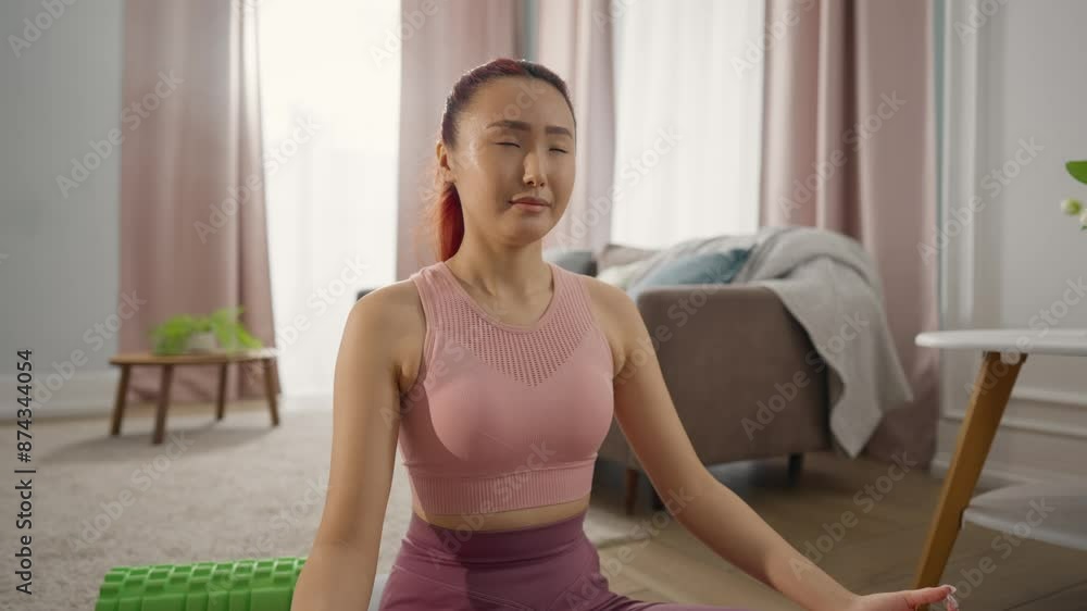 Asian girl practicing yoga alone at home in morning, peaceful face expression. Portrait of pretty Chinese young woman meditating in living room, calmness and peace, lady sitting in lotus position Asian girl practicing yoga alone at home in morning, peaceful face expression. Portrait of pretty Chinese young woman meditating in living room, calmness and peace, lady sitting in lotus position