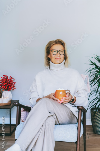 Foto Middle aged woman relaxing with pumpkin shaped cup of hot drink in scandy style hygge interior home with fall mood decor
