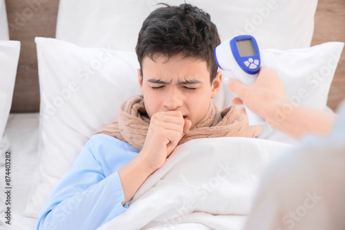 Mother with infrared thermometer measuring her ill son's temperature in bedroom, closeup