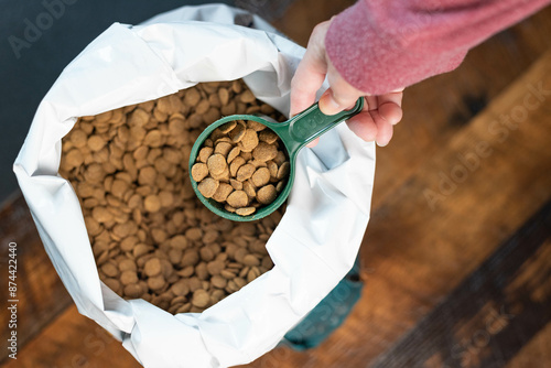 Hand removing a green measuring cup full of dog or cat food kibble from a white bag full of round pieces of food.