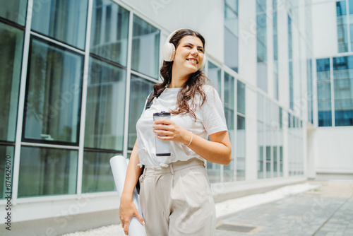 Free Download One young caucasian woman student going to university while listening to music on wireless headphones and holding papers and coffee	 - GFXLoad
