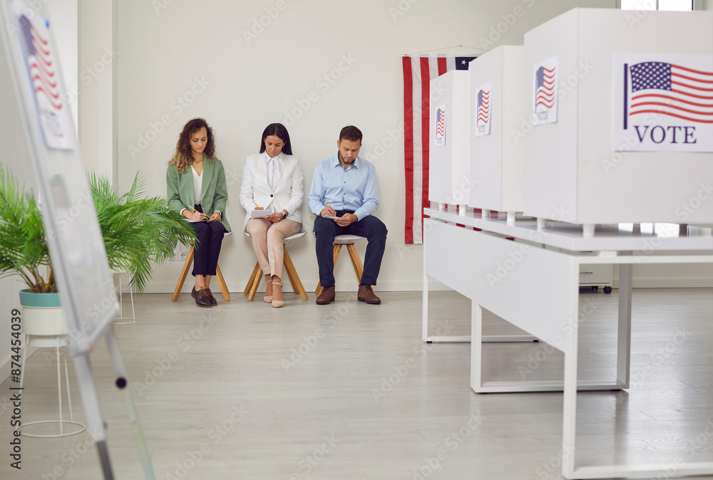 Fototapeta premium Polling station with a row of white voting booths decorated with American flag at vote center. People american voters sitting at polling station. Democracy and election day concept.