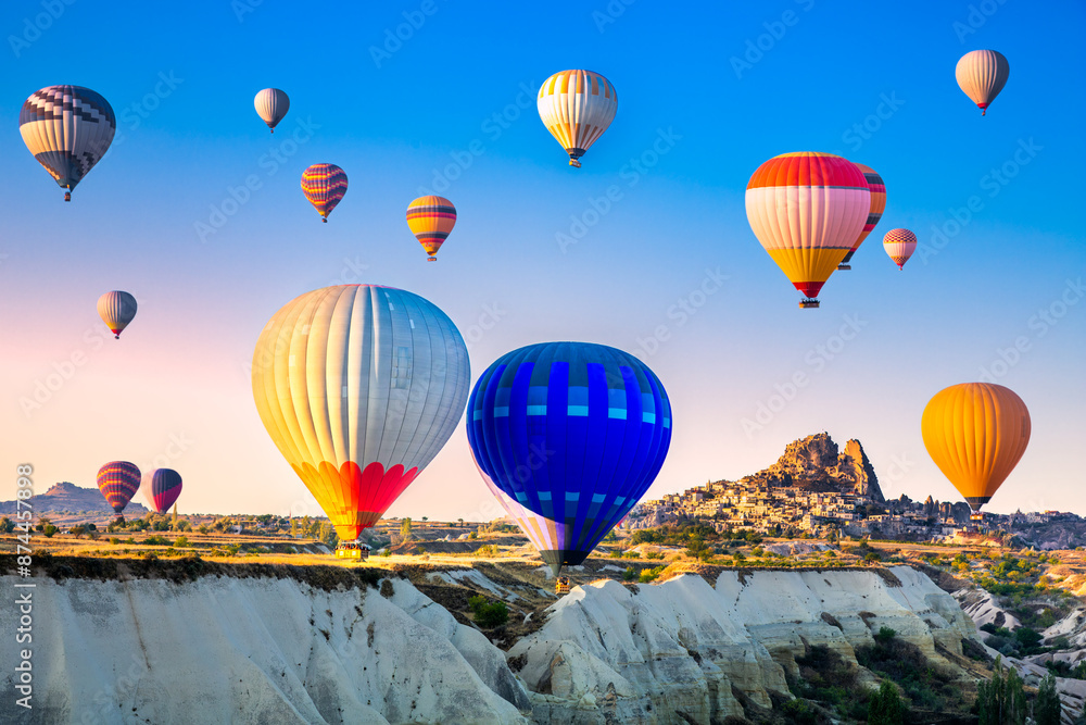 Aerial view of a fleet of hot air balloons with Uchisar Castle in the background, in Cappadocia, Turkey, at sunrise. Cappadocia is a popular tourist destination.