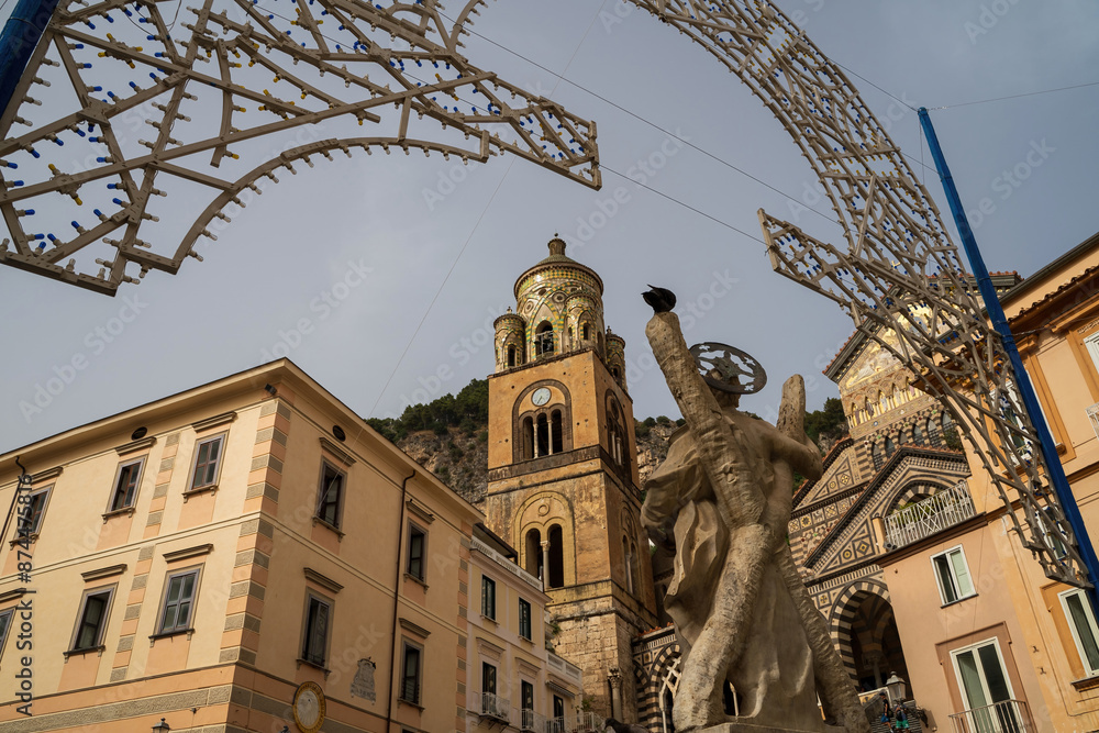 Rear view of a fountain statue located in the center of Amalfi against Cathedral bell tower in Amalfi, Italy. The church of the Apostle Saint Andrew, Roman Catholic church in the Piazza del Duomo