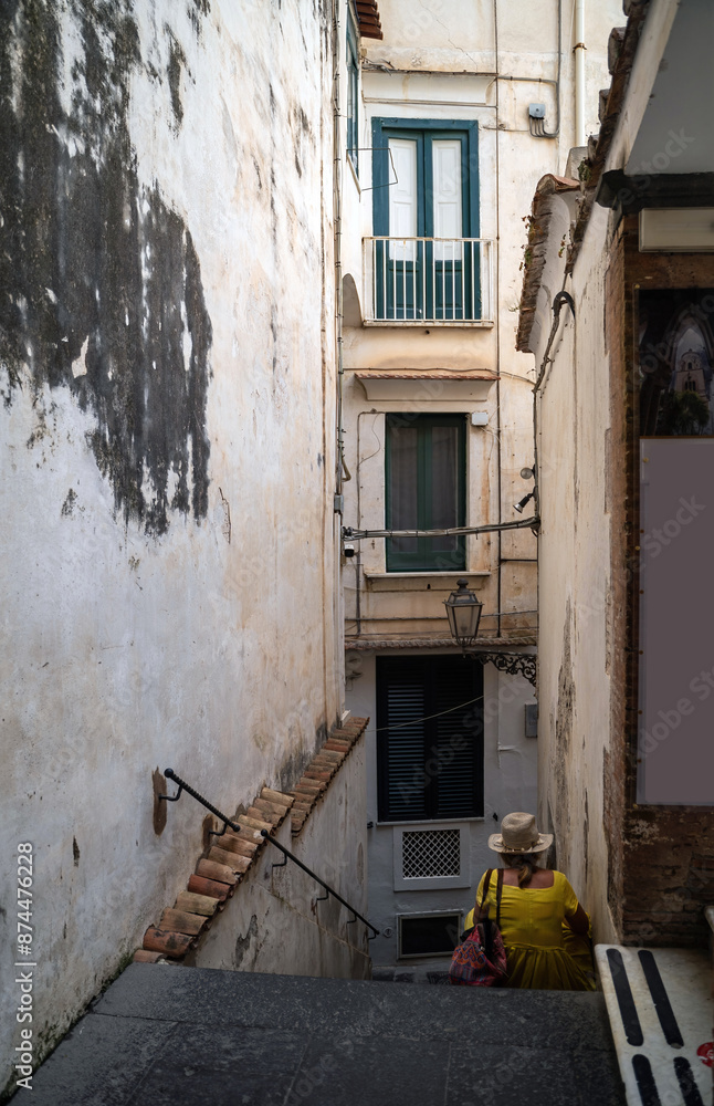 A rare view of an unidentified woman wearing a hat sitting on a stairs of a narrow street of Amalfi town, Southern Italy