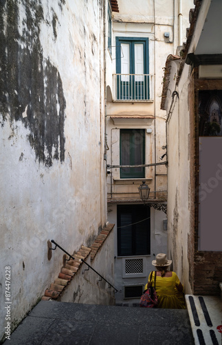 Obraz na płótnie A rare view of an unidentified woman wearing a hat sitting on a stairs of a narrow street of Amalfi town, Southern Italy w salonie