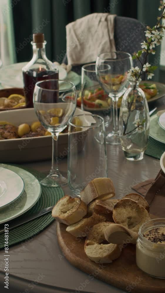 Medium vertical no people shot of table with homemade dishes in dining room of family home, with roast chicken, sliced bread, hummus or butter, wine glasses and cutlery Medium vertical no people shot of table with homemade dishes in dining room of family home, with roast chicken, sliced bread, hummus or butter, wine glasses and cutlery