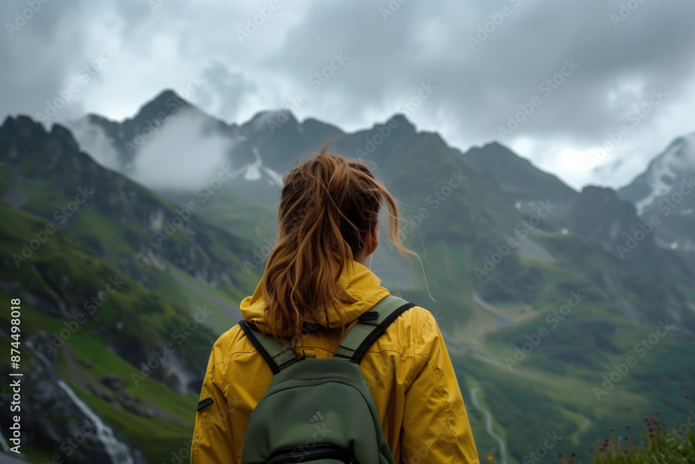A female traveler in a yellow jacket stands with her back to the camera, looking at the foggy mountain peaks. A female traveler in a yellow jacket stands with her back to the camera, looking at the foggy mountain peaks.