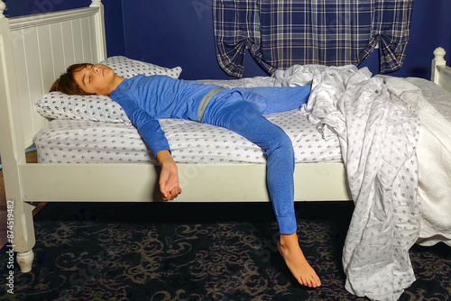 Preteen boy in blue pajamas asleep with one arm and leg hanging off the side of the bed