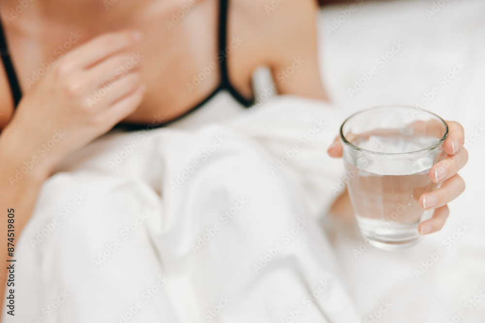 Woman laying in bed with a glass of water on top of a white comforter and sheet Woman laying in bed with a glass of water on top of a white comforter and sheet