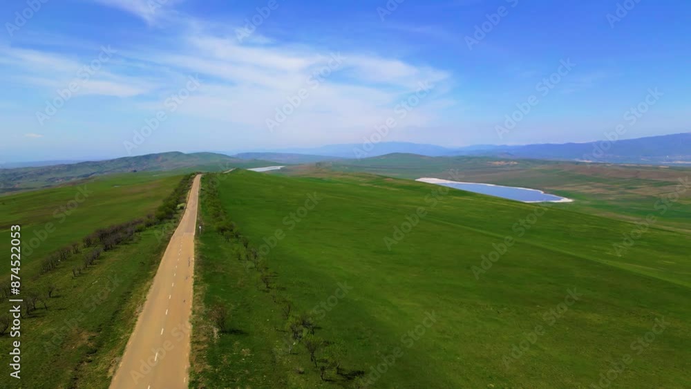 A summer landscape with green fields, a salty mountain lake, trees and a winding road under a clear blue sky, taken panoramically from a height A summer landscape with green fields, a salty mountain lake, trees and a winding road under a clear blue sky, taken panoramically from a height