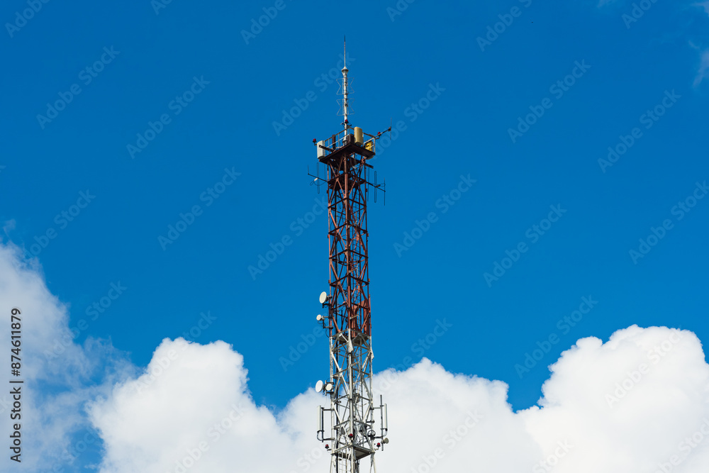 A tall metal tower stands against a bright blue sky, surrounded by puffy white clouds. The tower is a lattice structure, and it is topped with antennas and other equipment. A tall metal tower stands against a bright blue sky, surrounded by puffy white clouds. The tower is a lattice structure, and it is topped with antennas and other equipment.