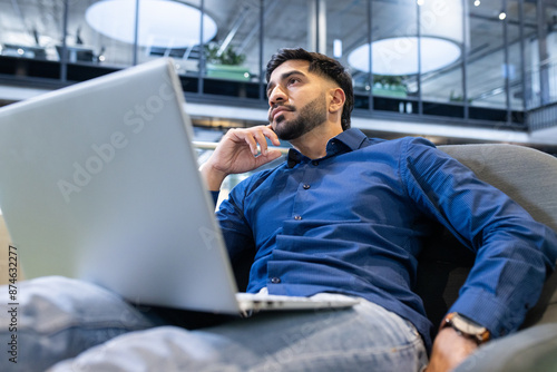 Thinking deeply, man working on laptop in modern office environment