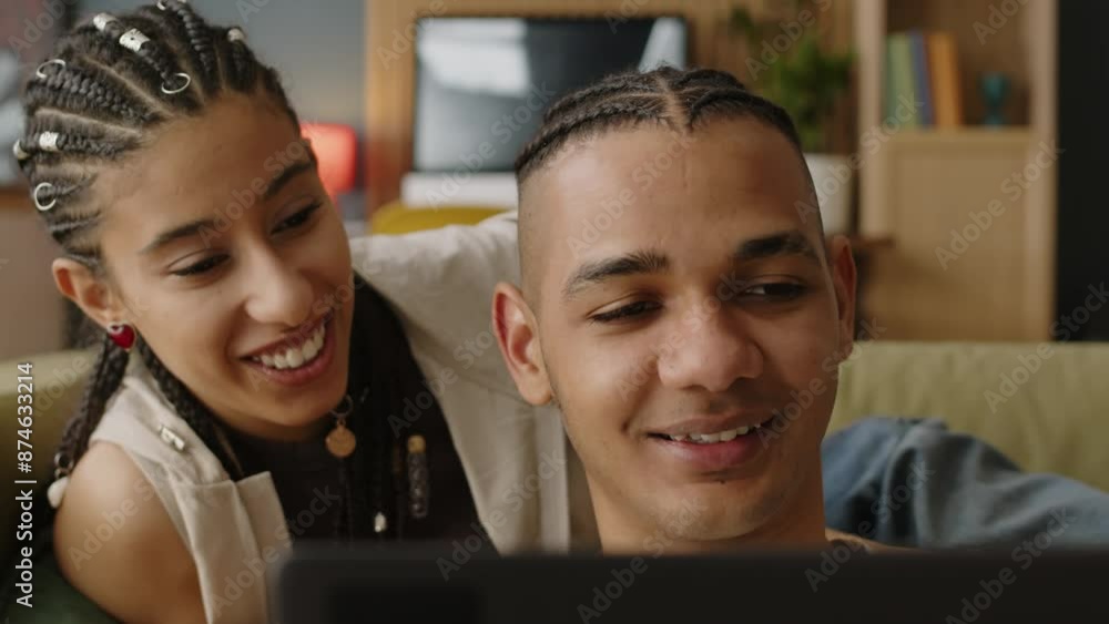 Chest up of cheerful Biracial girl laughing while watching her boyfriend playing game on laptop, living together in modern apartment Chest up of cheerful Biracial girl laughing while watching her boyfriend playing game on laptop, living together in modern apartment