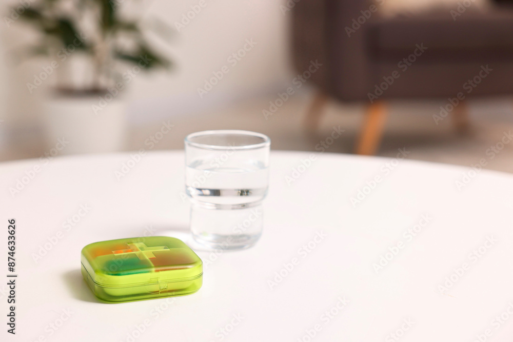 Different pills in organizer and glass of water at white table, closeup. Space for text Different pills in organizer and glass of water at white table, closeup. Space for text