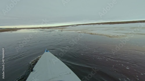 First-person view kayak paddling on an icy river in the Arctic. Ice floes and snow-covered banks line the waterway, highlighting the remote and challenging environment.