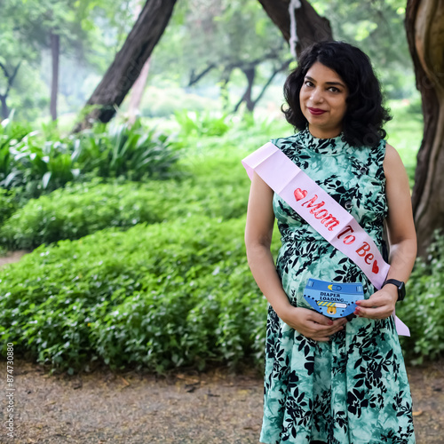 A pregnant Indian lady poses for outdoor pregnancy shoot and hands on belly, Indian pregnant woman puts her hand on her stomach with a maternity dress at society park, Pregnant outside maternity shoot photo