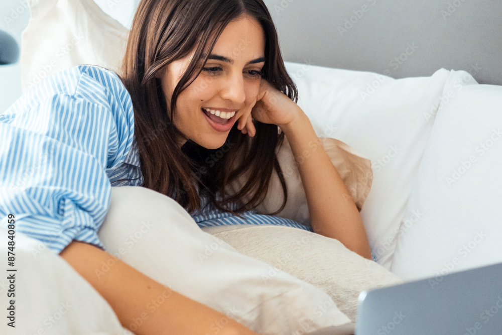 Smiling attractive woman lying on bed using laptop communicating online at home, happy girl typing on computer, enjoying internet shopping or chatting in social networks in modern cozy loft bedroom Smiling attractive woman lying on bed using laptop communicating online at home, happy girl typing on computer, enjoying internet shopping or chatting in social networks in modern cozy loft bedroom