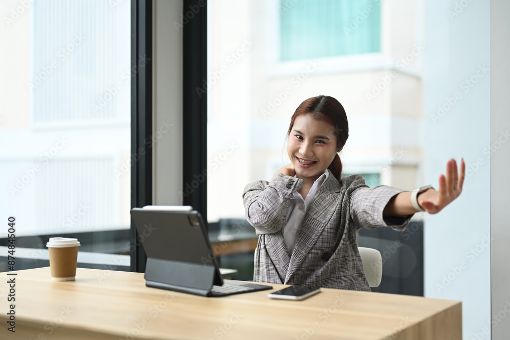 Happy relaxed young woman office worker sitting at desk with a laptop and stretching her arms Happy relaxed young woman office worker sitting at desk with a laptop and stretching her arms