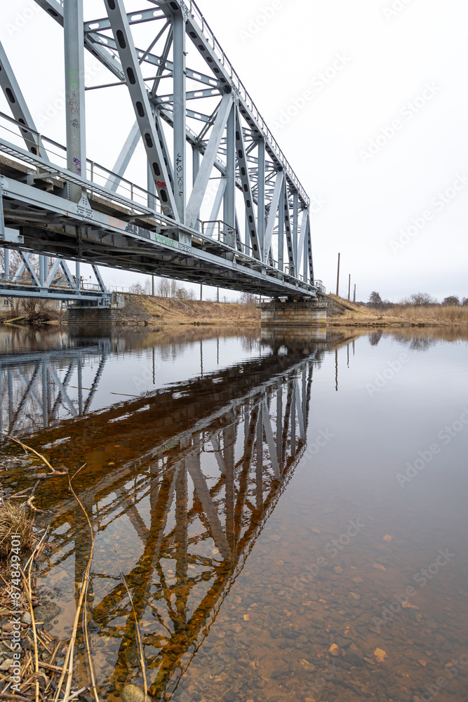 A metal truss bridge over the river in overcast spring day. Natural springtime scenery in Riga, Latvia. A metal truss bridge over the river in overcast spring day. Natural springtime scenery in Riga, Latvia.