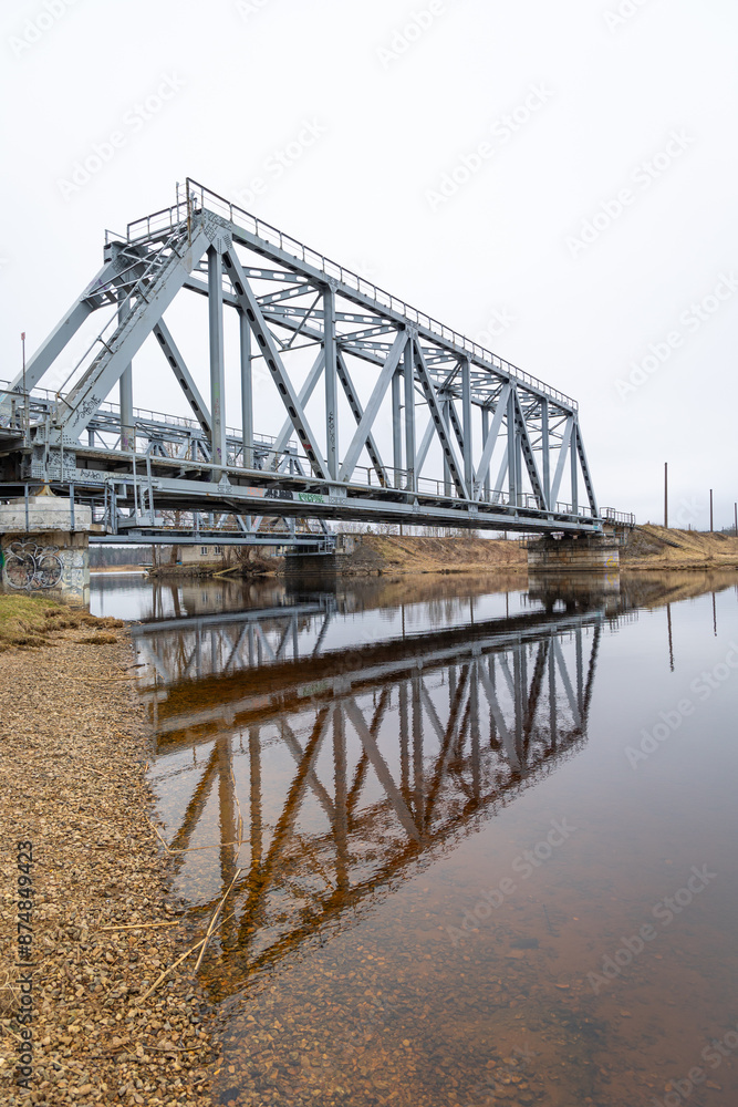 A metal truss bridge over the river in overcast spring day. Natural springtime scenery in Riga, Latvia. A metal truss bridge over the river in overcast spring day. Natural springtime scenery in Riga, Latvia.