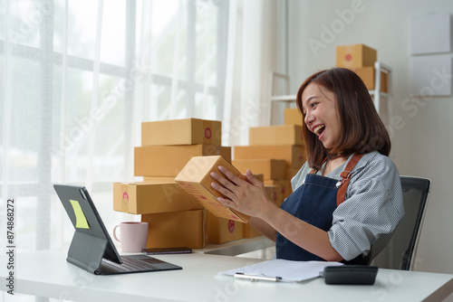 SME entrepreneurs, small businesses Online sales concept, happy Asian female business owner working on laptop computer and parcel boxes. Delivery of SME parcel boxes to customers Confirm order.