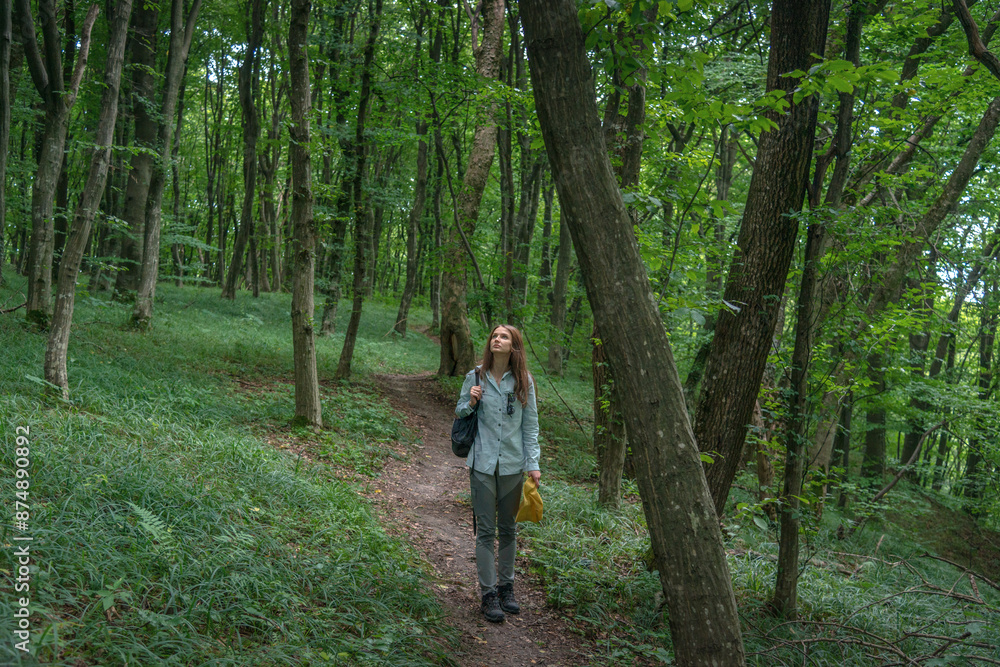 Young Woman Enjoying the Moments of Relaxation in a Forest. Cheerful woman in a yellow hat walking in the deep green forest. Enjoying fresh air and connection with nature. Young Woman Enjoying the Moments of Relaxation in a Forest. Cheerful woman in a yellow hat walking in the deep green forest. Enjoying fresh air and connection with nature.