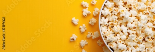 Delicious and crunchy popcorn scattered from a white bucket against a bright yellow background photo