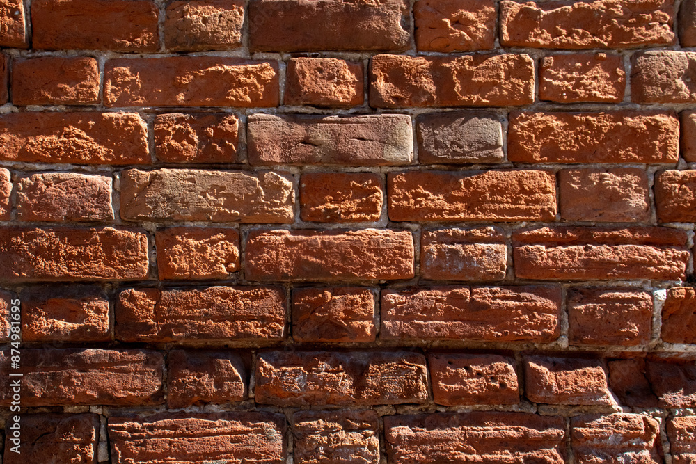 Obraz premium Fragment of a red brick wall, close-up. The texture of brick, battered by wind and rain. Old bricks in the wall of a building.