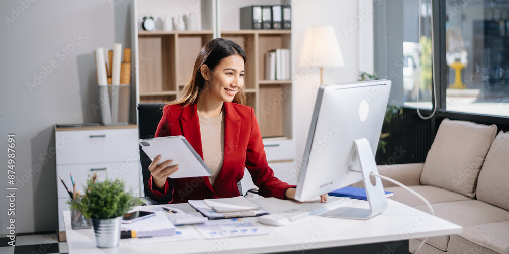 Young beautiful woman typing on tablet and laptop while sitting at the working white table in modern office Young beautiful woman typing on tablet and laptop while sitting at the working white table in modern office