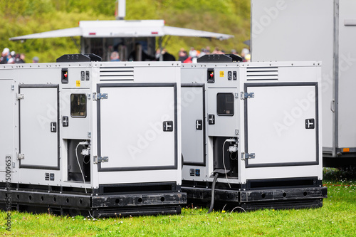 Set two large portable industrial power fuel generator green lawn at commercial event outdoors clear blue sky background. Mobile electricity supply energy plant unit backup equipment rent service