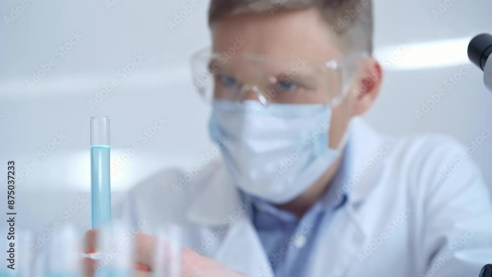 Man with safety glasses and blue mask is working with lab tubes using a pipette in a modern laboratory, close-up of researcher. Science and medicine Man with safety glasses and blue mask is working with lab tubes using a pipette in a modern laboratory, close-up of researcher. Science and medicine