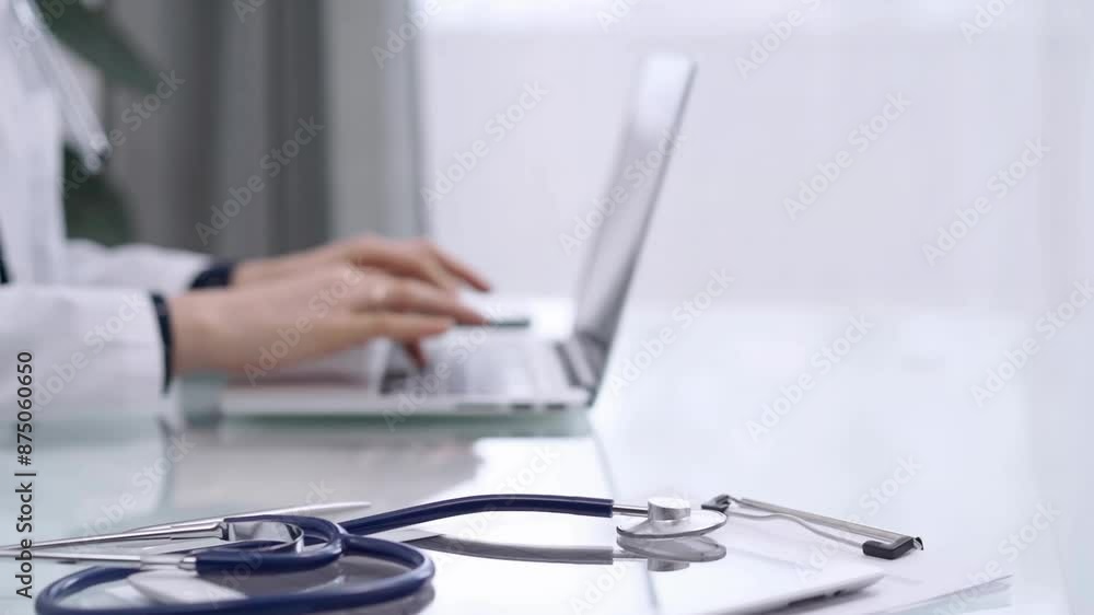 Stethoscope and medical clipboard are lying on the glass table while doctor woman is working with laptop computer on the background. Medicine and pharmacy concept Stethoscope and medical clipboard are lying on the glass table while doctor woman is working with laptop computer on the background. Medicine and pharmacy concept